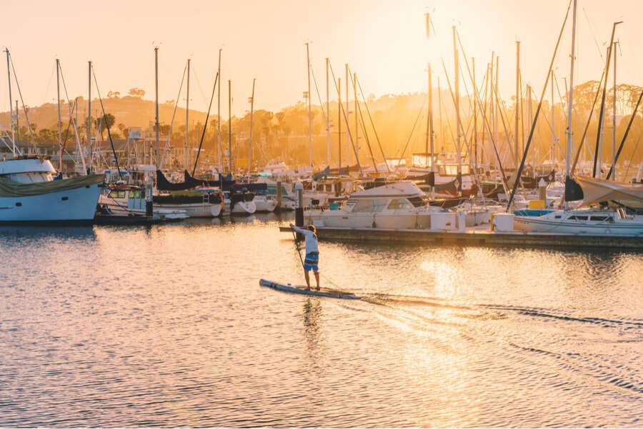 Paddleboarder gliding across a calm harbor in low golden sunlight